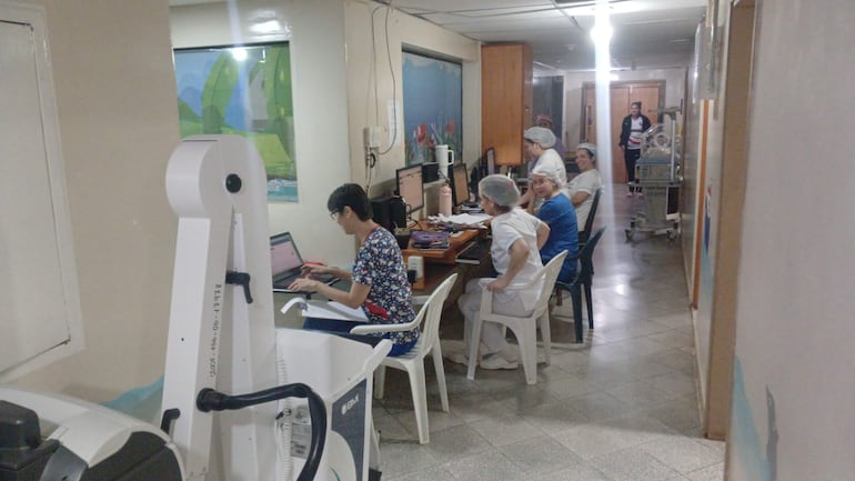 Cinco médicos en un ambiente clínico, concentrados en computadoras. Sonríen y colaboran en un entorno de trabajo activo.