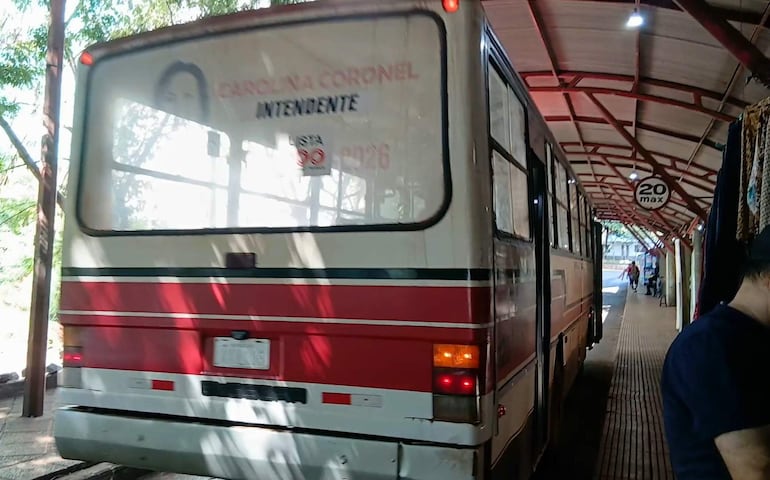 Autobús blanco y rojo de Carolina Coronel en terminal, con señal de límite de velocidad y peatones al fondo.
