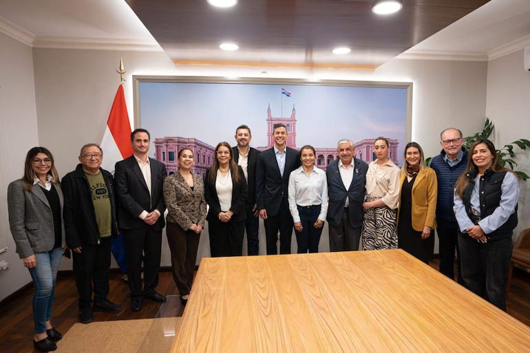 Santiago Peña y miembros de Sinamed sonríen en reunión formal, con bandera paraguaya y mural de fondo.