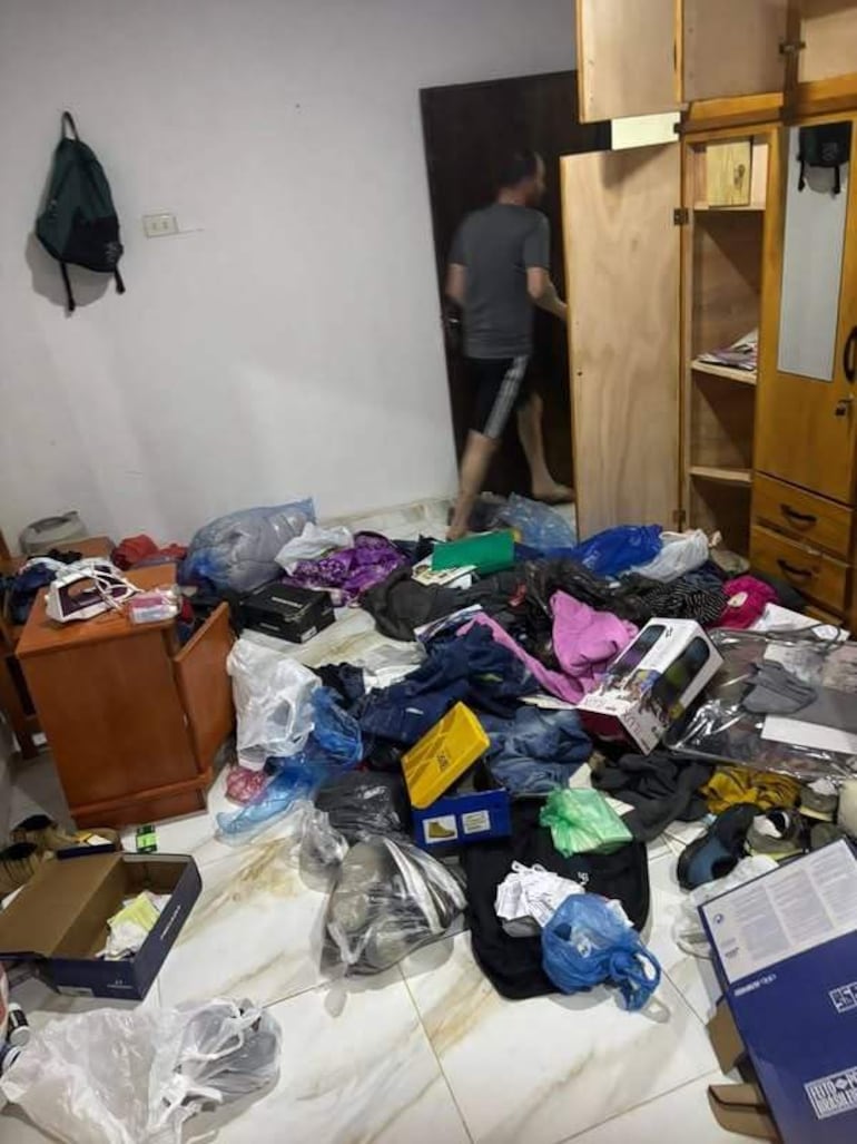 Hombre de espaldas en habitación desordenada, con camiseta y pantalones cortos, preparándose para salir.