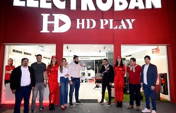 Hamza Damani habla frente a varias personas, con tres mujeres en trajes rojos destacándose en un ambiente urbano y comercial.