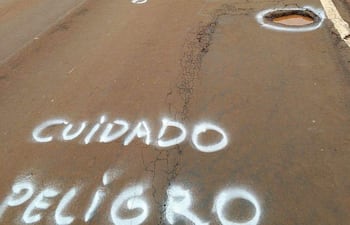 Carretera con agujeros y señalización de peligro en spray. No hay personas presentes en la escena.