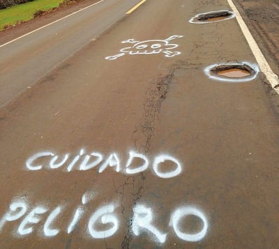 Carretera con agujeros y señalización de peligro en spray. No hay personas presentes en la escena.