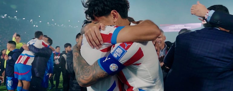 Jugadores de Club Nacional abrazándose en un estadio, visiblemente emocionados y con camisetas blancas y rojas, rodeados de confeti.