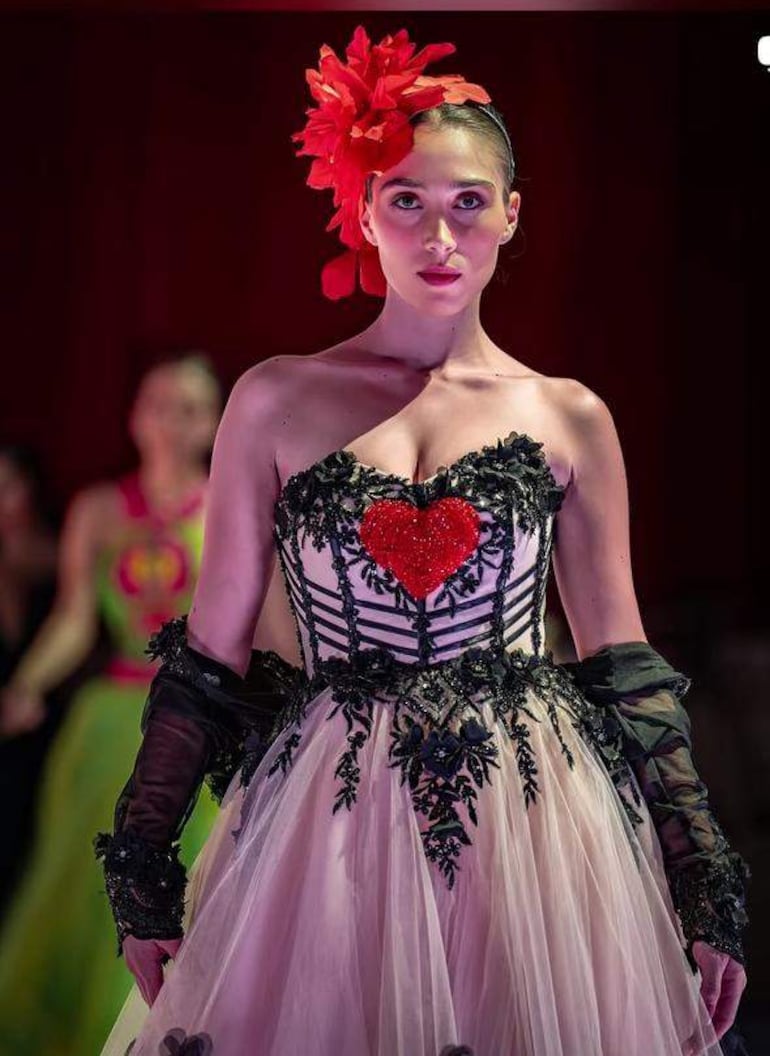 Natasha Reckziegel Griebeler en el centro del escenario, vestida con un elaborado vestido que incluye un corpiño con un corazón rojo brillante.