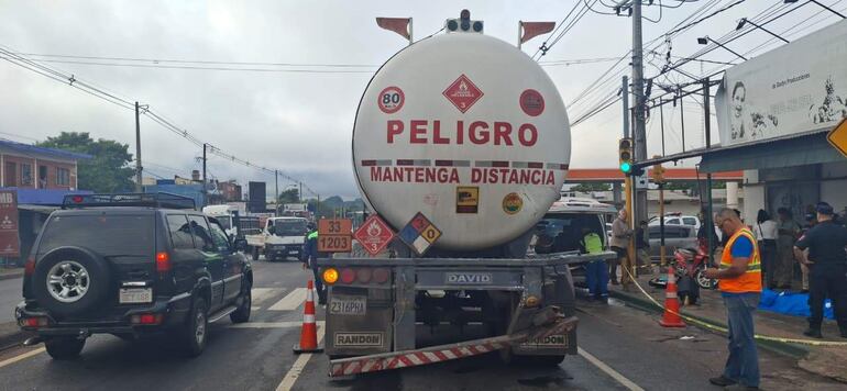 Camión cisterna con señal de advertencia estacionado en el cruce semafórico. Varias personas observan el incidente.