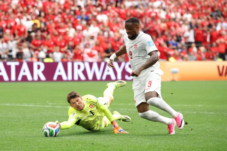El portero suizo Gregor Kobel hace el esfuerzo por desviar el balón ante la presencia de Cyle Larin.  