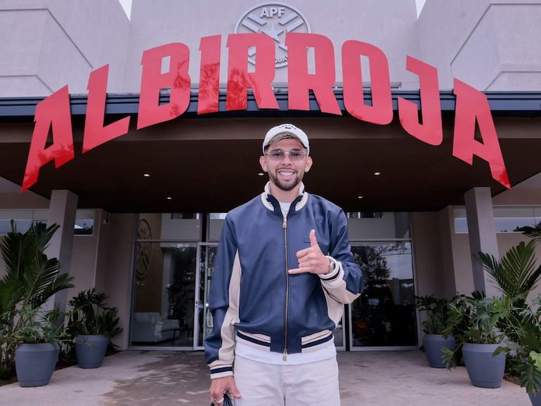 Julio Enciso sonríe con chaqueta y camiseta blanca, junto al letrero 'ALBIRROJA' en la APF. Plantas decorativas en el entorno.