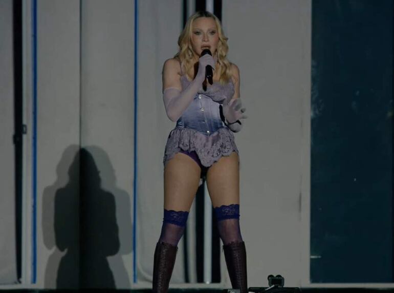 Madonna viste pantalones cortos, cantando enérgicamente en el escenario de Coachella, bajo luces brillantes en un ambiente festivo.