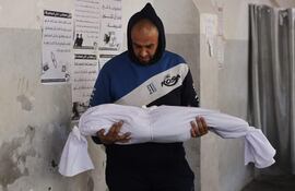 Un palestino con el cadáver de un niño muerto en ataques aéreos israelíes nocturnos en la ciudad de Gaza, 12 de diciembre de 2024 (AFP)