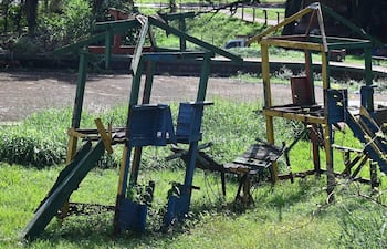 Estructuras de juego de madera en área verde deteriorada, sin personas presentes y césped alto.