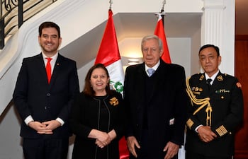 Cuatro personas en un evento formal: hombre con traje oscuro y corbata roja, mujer en vestido negro, hombre mayor con abrigo oscuro y militar en uniforme.