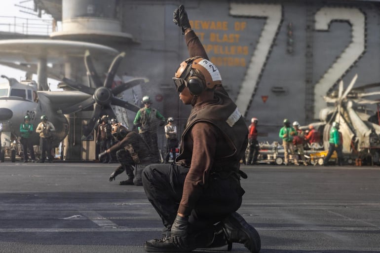 Un capitán de ala aérea señala durante las operaciones de vuelo a bordo del USS Abraham Lincoln (CVN 72). Los capitanes de avión, que visten camisas marrones, son responsables de la seguridad e integridad de las aeronaves, incluyendo la preparación previa y posterior al vuelo. (Red social X de Cent Com)