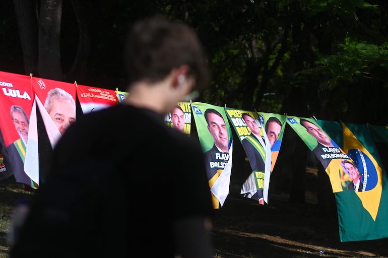 Un hombre camina frente a una tienda informal de banderas con la imagen del presidente de Brasil y candidato a la reelección, Luiz Inácio Lula da Silva y del candidato presidencial, Flávio Bolsonaro.