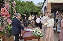Ricardo Flecha de traje oscuro habla a la audiencia, mientras Fanny Pereira sostiene un ramo de flores, rodeados de decoraciones florales.