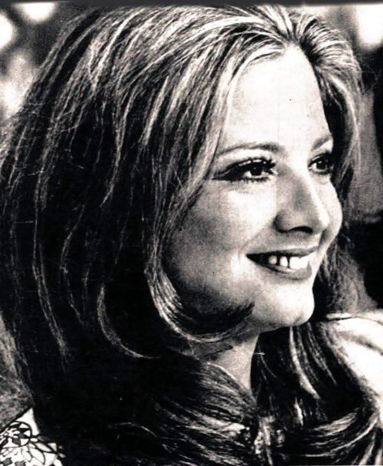 Gloria Menezes sonriendo, con fondo neutro, mostrando una expresión feliz y vestimenta sencilla.