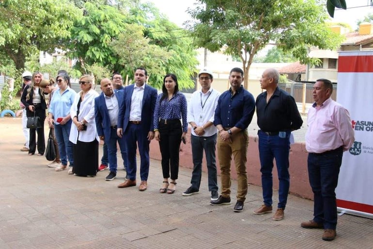 Luis Bello y otros asistentes en evento formal, todos vestidos con trajes y atuendos semi-formales, mostrando expresión tranquila.