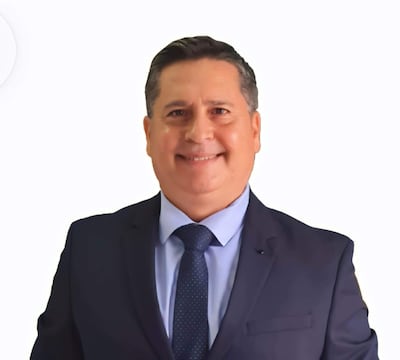 Juan Martín Palacios Fantilli sonríe con abrigo y corbata en ambiente formal, acompañado de otros asistentes.