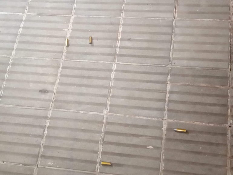 Suelo de baldosas grises con cuatro cartuchos de balas esparcidos, sin personas presentes en la escena.