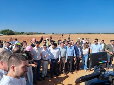 Santiago Peña en casco con gestos de presentación ante un grupo de personas vestidas semi-formalmente en un evento al aire libre.