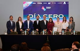 Elías Saba en conferencia, rodeado de personas de pie con expresiones tranquilas, en un salón decorado con sobriedad.