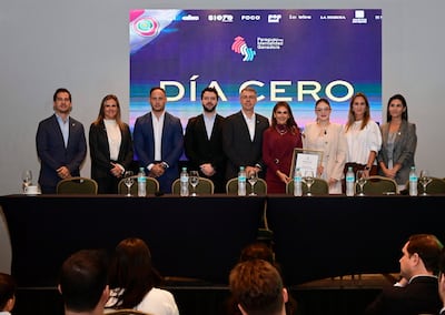 Elías Saba en conferencia, rodeado de personas de pie con expresiones tranquilas, en un salón decorado con sobriedad.