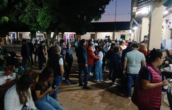Mujer sentada con teléfono, mientras otros conversan en un ambiente festivo con luces artificiales.