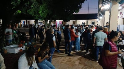 Mujer sentada con teléfono, mientras otros conversan en un ambiente festivo con luces artificiales.