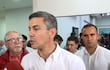 Santiago Peña en camisa blanca frente a micrófono rojo, rodeado de personas en un ambiente formal, algunos observando atentamente.