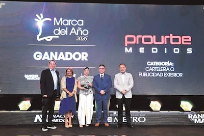 Grupo de cinco personas en premiación, hombre con chaqueta oscura sostiene un premio junto a mujer en blusa azul y otros en traje.