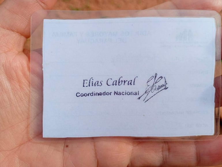 Una mano sostiene una tarjeta de identificación con el nombre Elías Cabral y el título Coordinador Nacional, sobre un fondo natural.