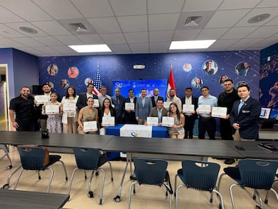 Estudiantes sosteniendo diplomas en un aula, con expresiones alegres, en un ambiente decorado con banderas.
