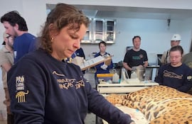 Mujer con guantes y camiseta de 'Projeto Onças do Iguaçu' atiende a un yaguareté recostado en una mesa mientras otros observan.