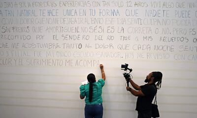 Una víctima mientras escribe unas líneas de un poema, en el muro de Fragmentos para la exposición "Desamadas", como reparación simbólica de las atrocidades sufridas en el conflicto armado.