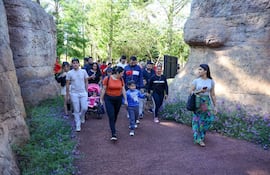 Grupo de 15 personas, incluidos niños, caminan entre vegetación, algunos conversando, otros concentrados en el sendero.