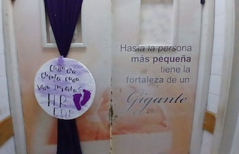 Letrero decorativo en puerta de hospital con mensaje sobre el valor de la vida, fondo claro y cortina negra.