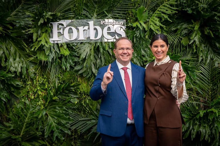Camilo Pérez y Costanza Troche sonríen, levantando el dedo índice, con fondo de vegetación y letrero de Forbes Paraguay.