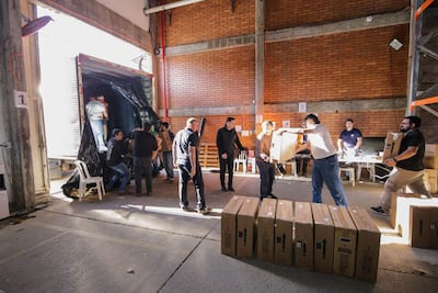 Personas trabajando en almacén, desempacando cajas de un camión mientras la luz natural ilumina el lugar.