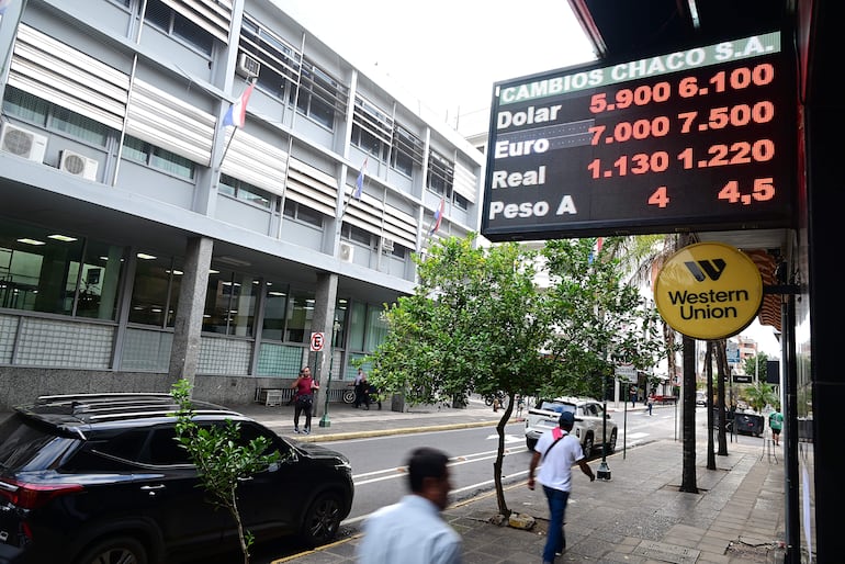 Una mujer y dos hombres en la acera, uno con camiseta blanca y sombrero, otro con camiseta roja, frente a un edificio comercial.