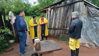 Grupo de cinco personas en chaquetas oscuras y amarillas en conversación frente a una construcción de madera en el campo.