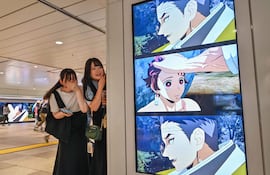 Dos jóvenes miran a una amiga mientras permanecen junto a una cartelera digital que anuncia el próximo lanzamiento del videojuego “Demon Slayer: Kimetsu no Yaiba – The Hinokami Chronicles 2”, a lo largo de un pasillo dentro de una estación de tren en el centro de Tokio, el 29 de julio de 2025.
