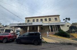 Hombre de pie frente a la edificación de dos pisos del centro médico, donde se observa un letrero de 'URGENCIAS'.