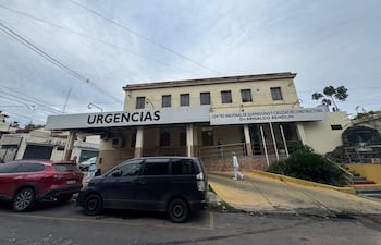Hombre de pie frente a la edificación de dos pisos del centro médico, donde se observa un letrero de 'URGENCIAS'.
