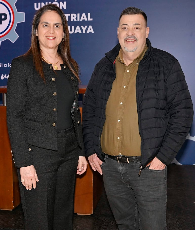Mujer de cabello largo en vestido negro y hombre con chaqueta negra sonríen en evento de la Unión Industrial del Paraguay.