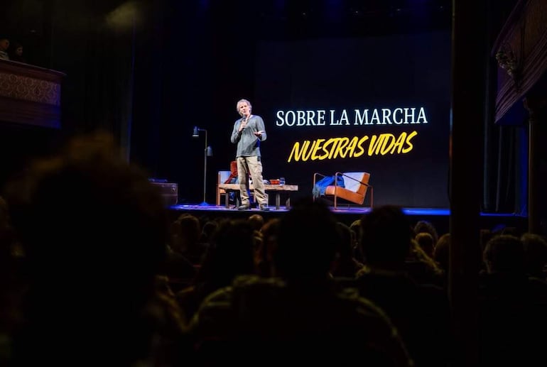 Facundo Arana con camiseta azul gesticula mientras habla frente a una audiencia atenta en un teatro con buena iluminación.