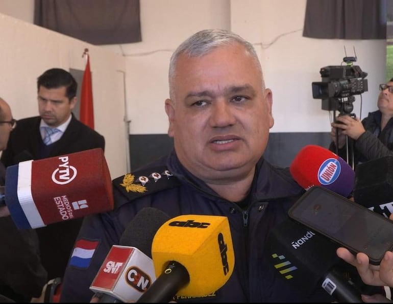 Héctor Fernández, con uniforme de policía, habla a varios micrófonos, mientras otra persona en traje escucha atentamente.