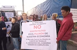 Hombre con micrófono y mujer con pancarta sobre economía, en una protesta en exteriores del Mercado de Abasto.