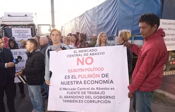 Hombre con micrófono y mujer con pancarta sobre economía, en una protesta en exteriores del Mercado de Abasto.