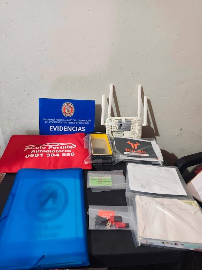 Mesa con objetos diversos, incluyendo un cartel azul que dice 'EVIDENCIAS', paquetes con dispositivos electrónicos y documentos.