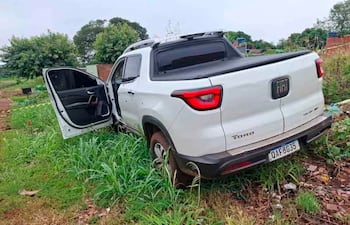 Camioneta Fiat Toro blanca estacionada en pastizales con puerta abierta, sin personas visibles.
